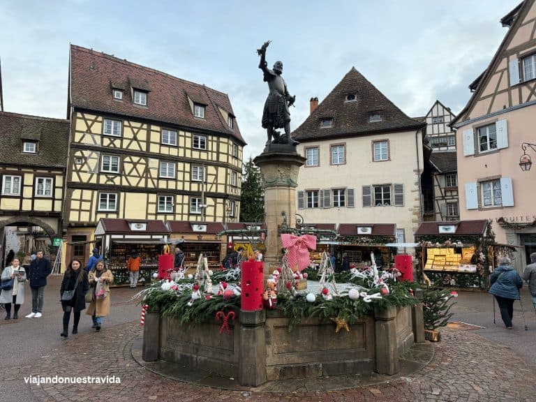 Colorful Christmas market in a historic European town square with festive decorations and old buildings.