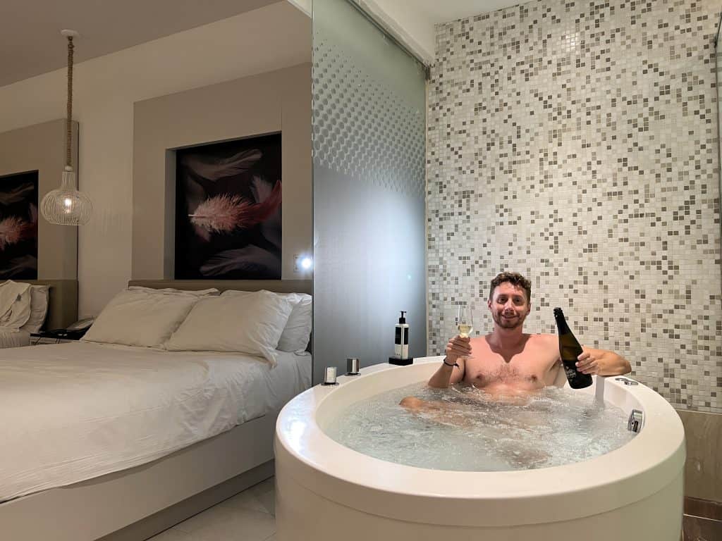 Relaxing man with a drink in a bubble bath at a stylish hotel room.