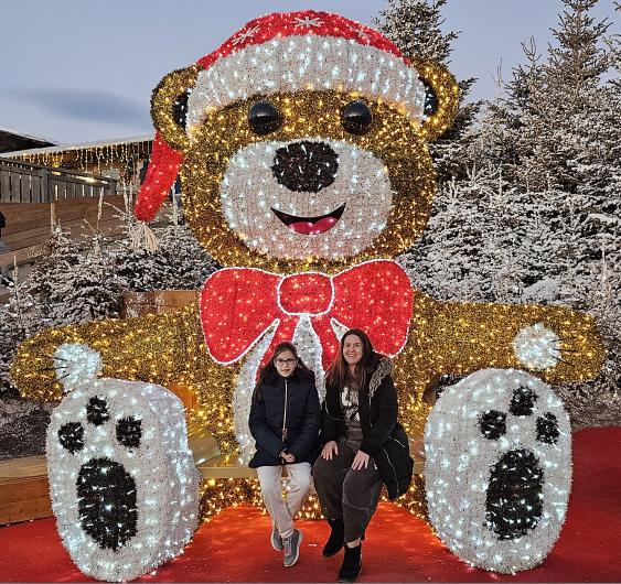 Bright illuminated Christmas bear decoration with two women posing outdoors at night.