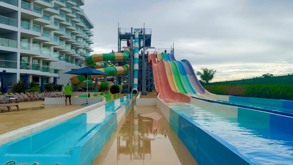 Colorful water slides at a tropical resort with a modern hotel in the background.