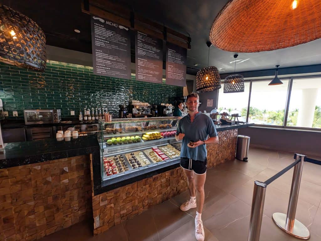 A man choosing desserts at a modern café with green tiled wall and large window view.