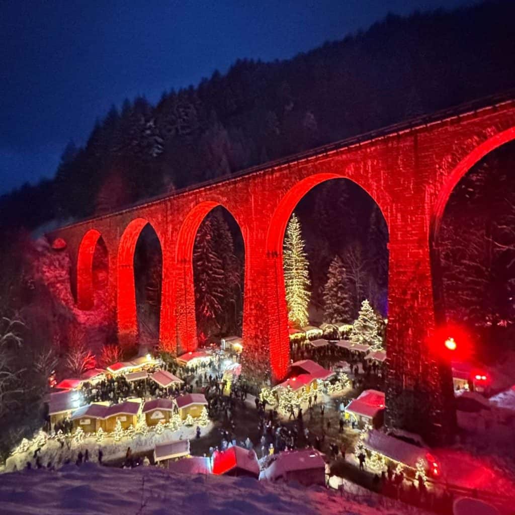 Vibrant red-lit historic railway viaduct illuminated at night during winter festival.