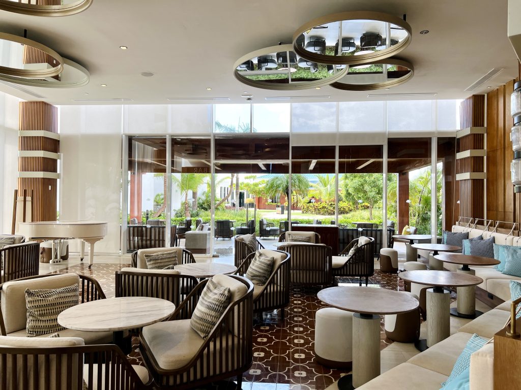 Salón del lobby bar del Dreams Cap Cana, con mesas y ventanales al jardín