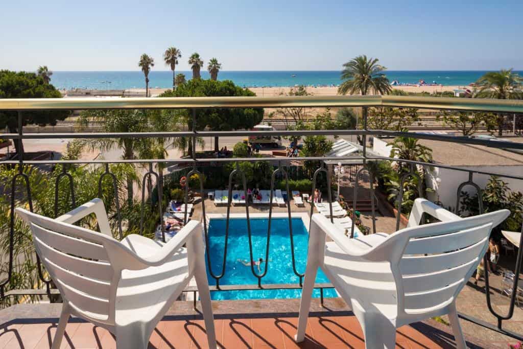 Beach view from a hotel balcony with pool and palm trees.