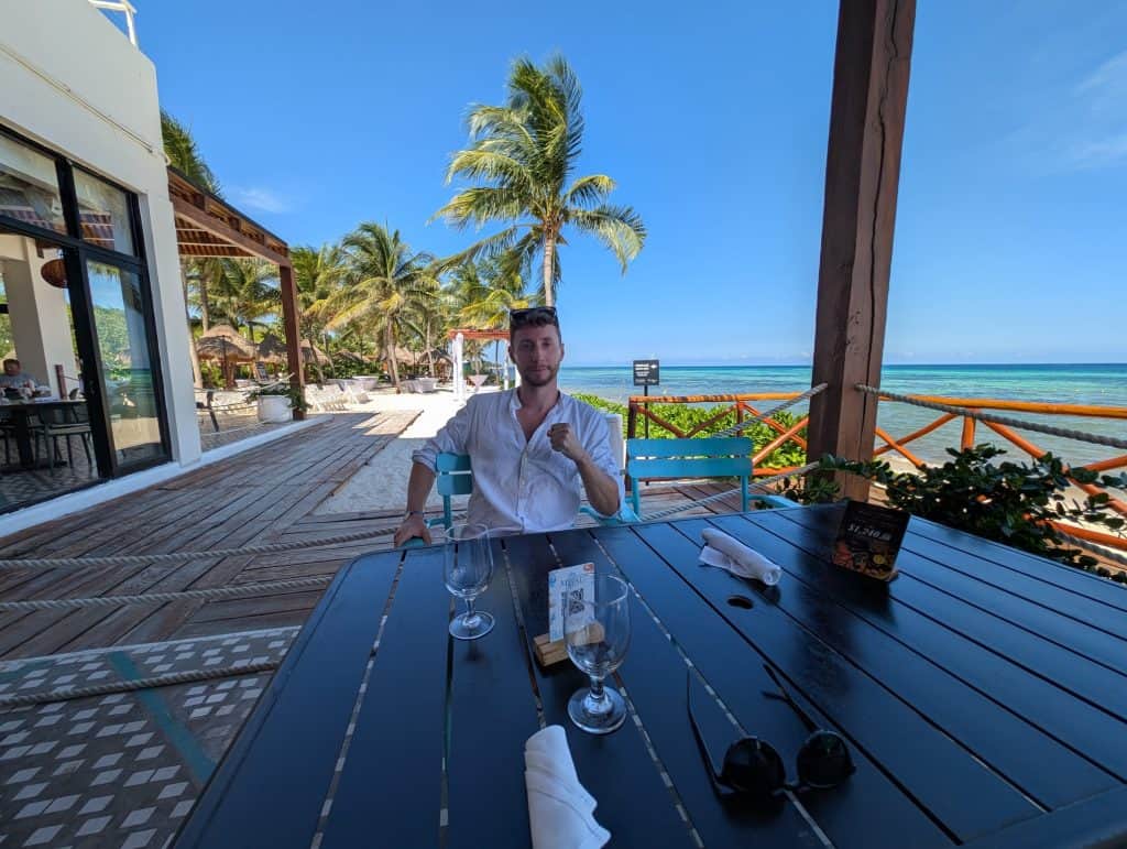 Relaxed man dining on an outdoor seaside terrace with palm trees and ocean view.