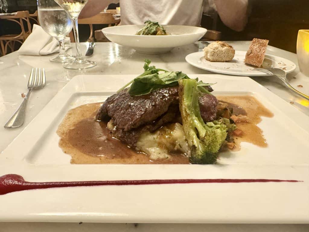Succulent steak with vegetables and gravy served on a white plate at a fancy restaurant.