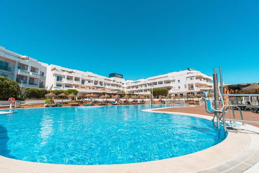 Bright hotel pool with white building and blue sky, sunny vacation setting.
