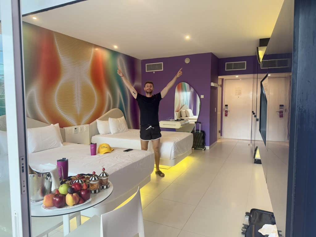 Colorful hotel room with vibrant wall art, modern decor, and a cheerful guest celebrating.