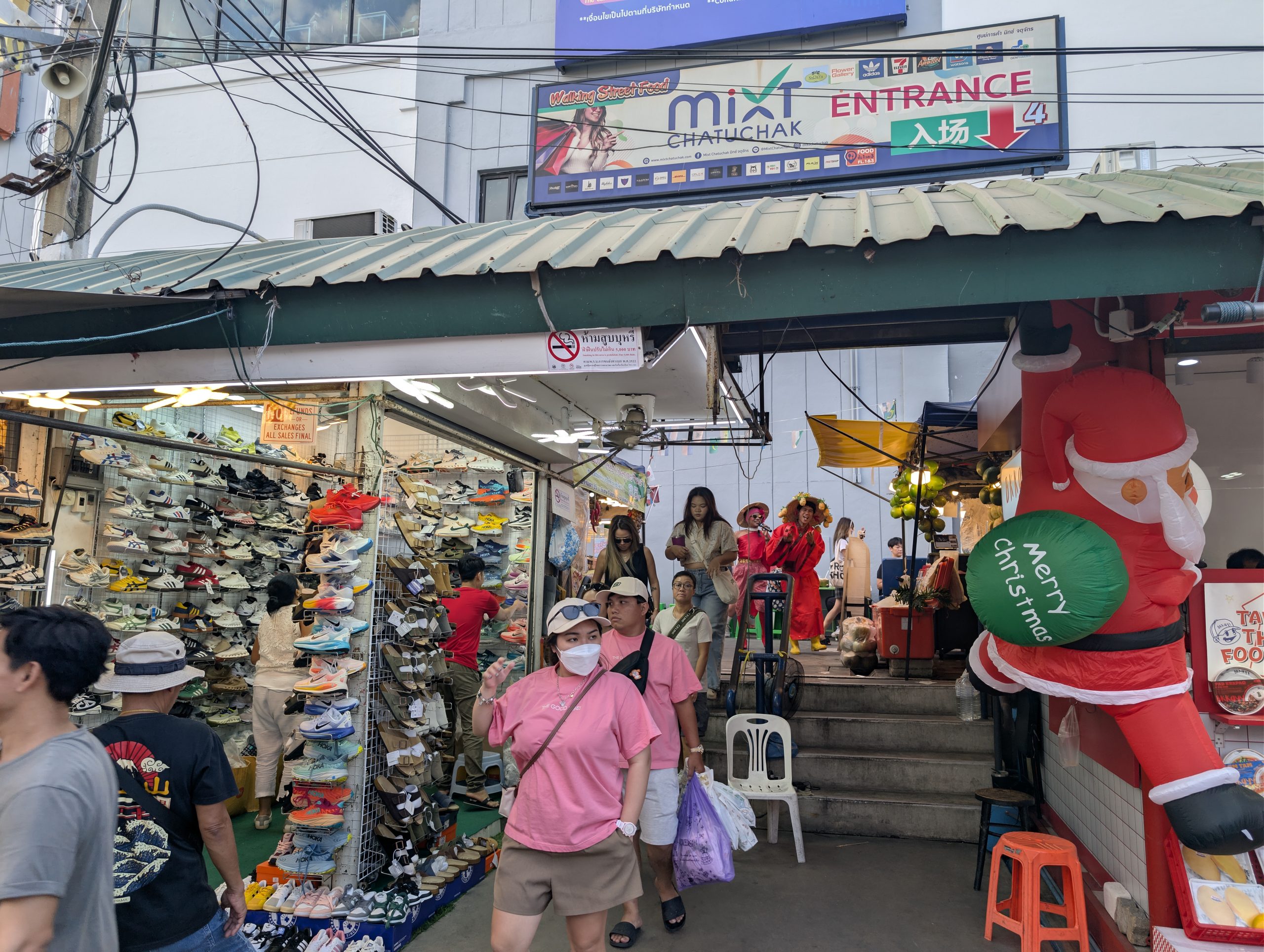 Una de las entradas del mercado de Chatuchak en Bangkok, con los puestos de zapatillas y la gente pasando bajo el cartel
