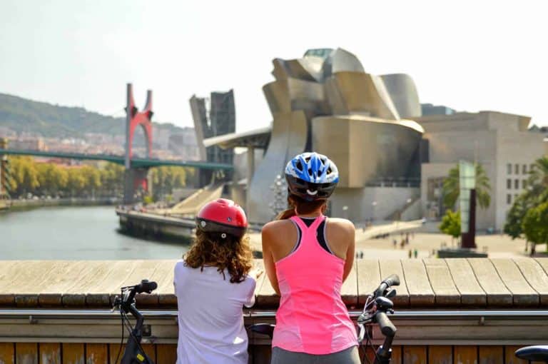 A woman and a girl with bicycles overlooking the Guggenheim Museum Bilbao in Spain.