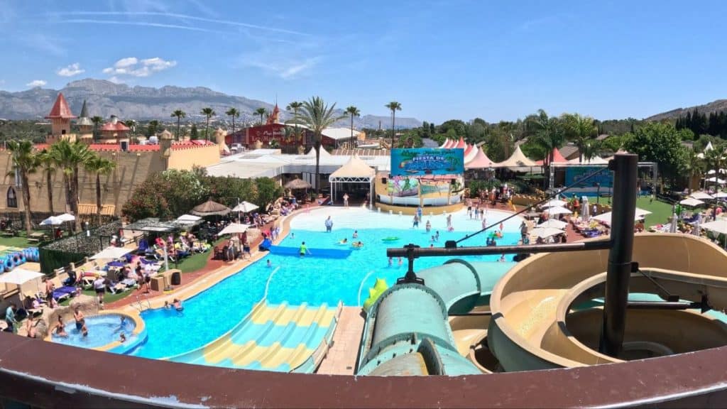 Water slide and swimming pool at a tropical resort with mountains in the background.