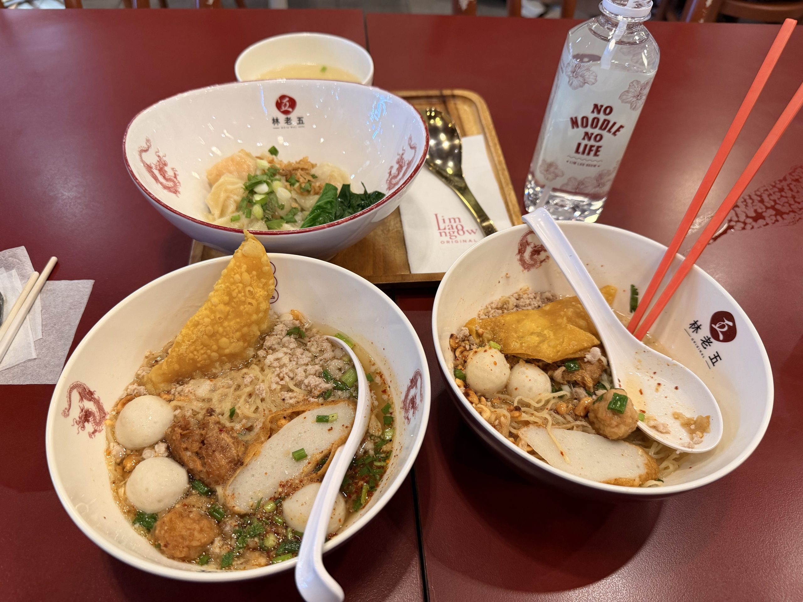 Dos cuencos de fideos de Lim Lao Ngow con albóndigas de pescado y wonton frito, junto a la botella con el lema No Noodle No Life