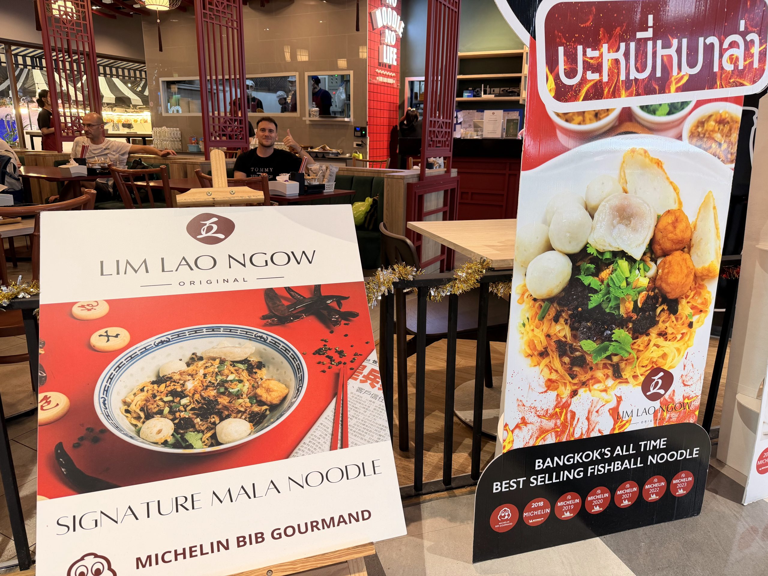 Carteles de Lim Lao Ngow en el MBK con el sello Michelin Bib Gourmand y el Signature Mala Noodle