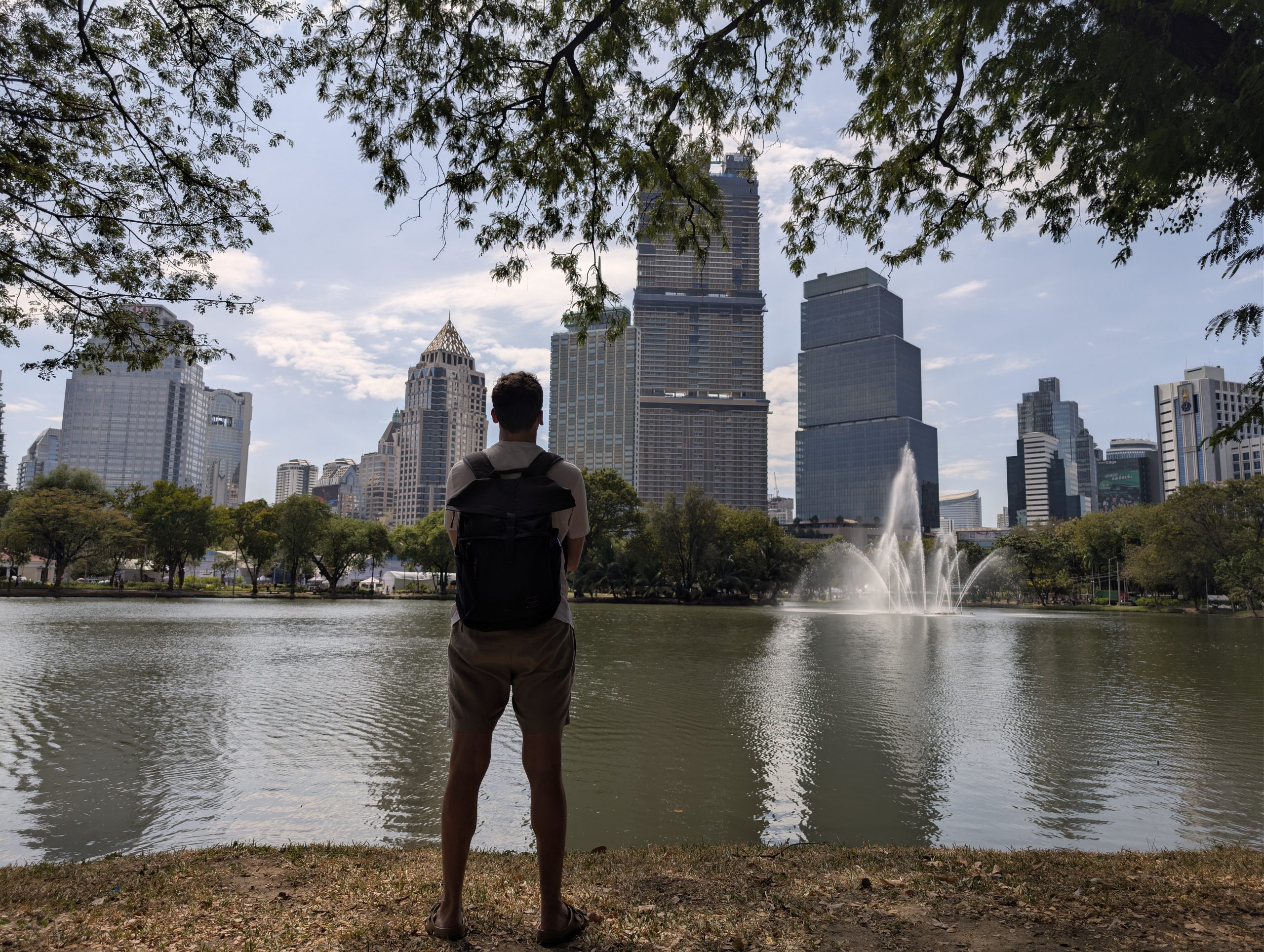 Víctor de espaldas mirando el lago del parque Lumphini de Bangkok, con la fuente y los rascacielos de Silom al fondo