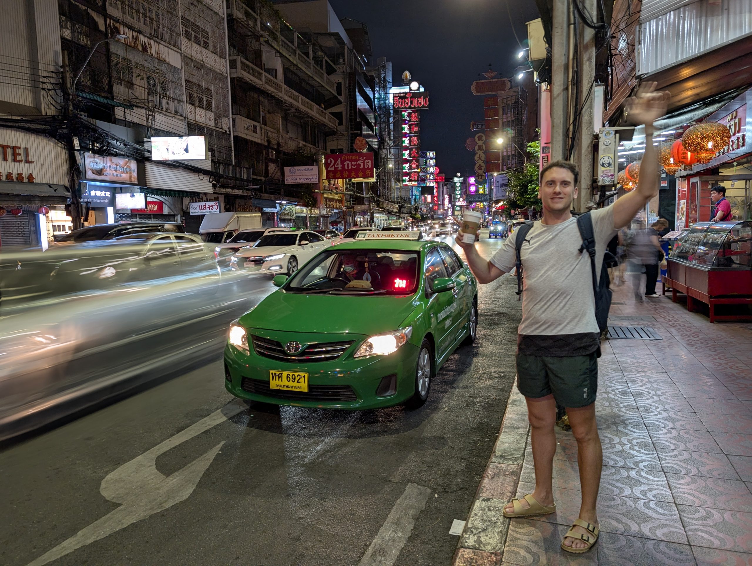 Víctor parando un taxi verde con el cartel de Taxi Meter en una calle de Chinatown en Bangkok de noche