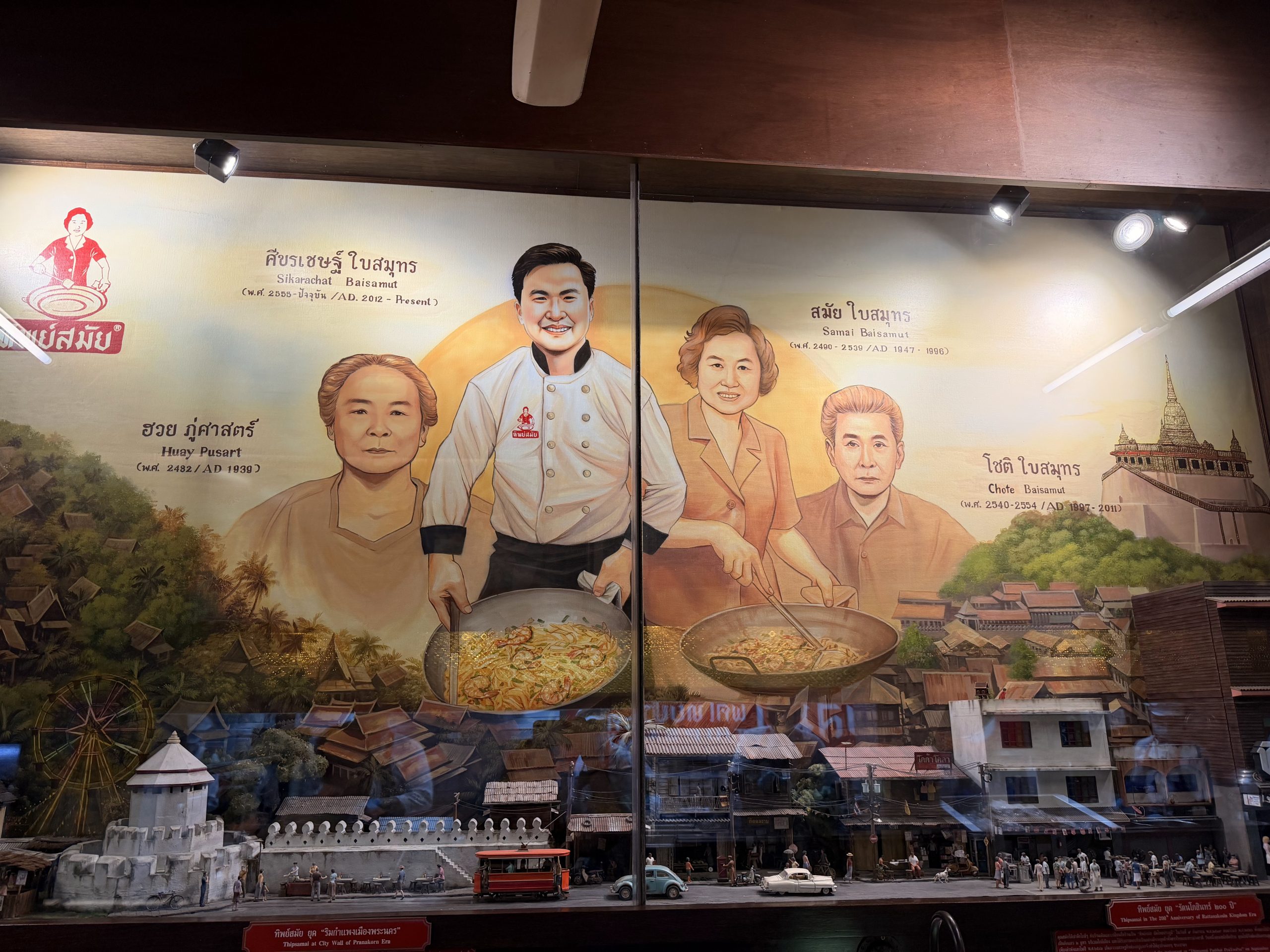 Mural de Thipsamai con los retratos de las cuatro generaciones de la familia fundadora y una maqueta del Bangkok antiguo debajo