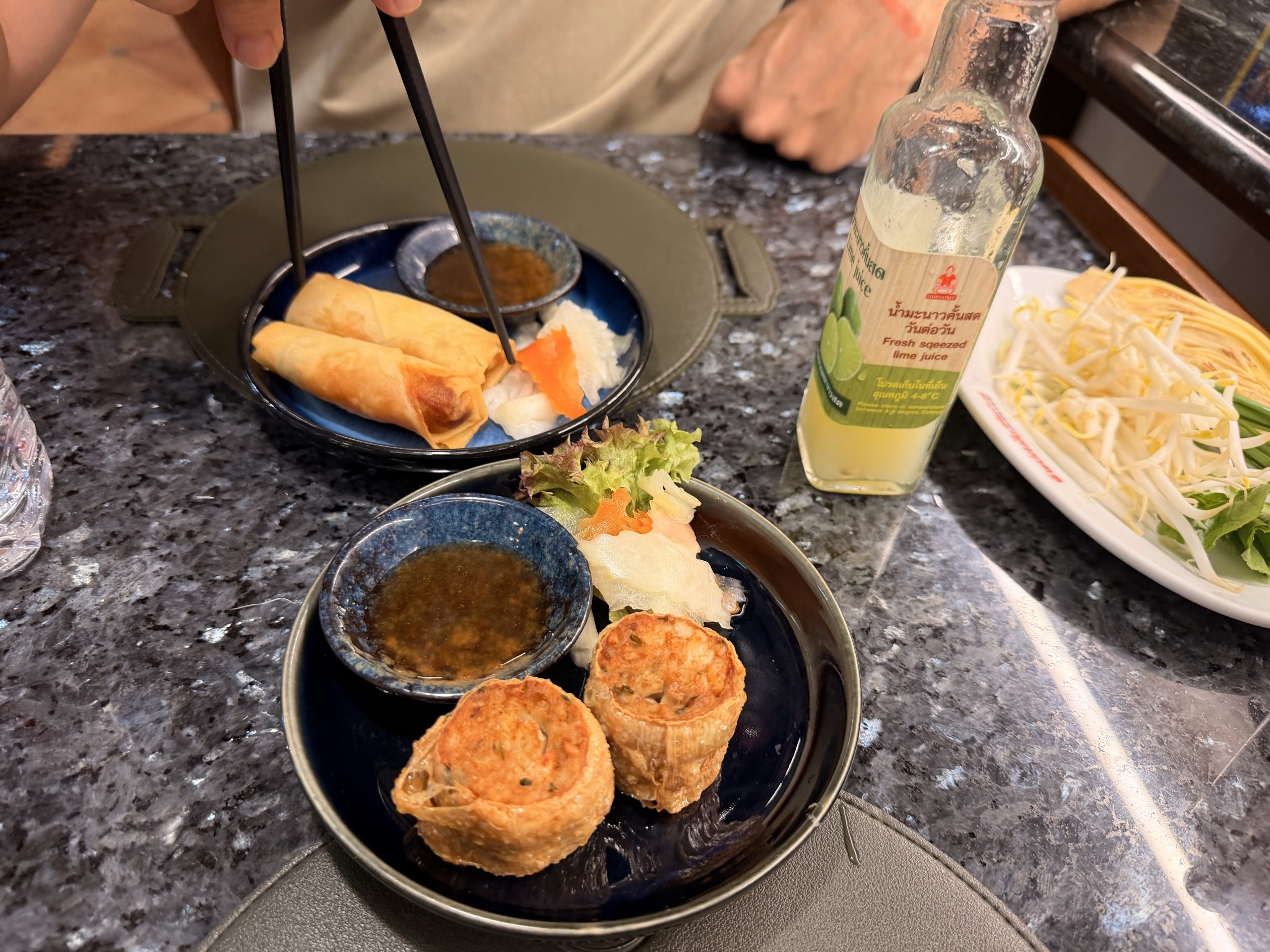 Entrantes fritos de Thipsamai, rollitos y bolas de gambas, con salsa, brotes de soja y una botella de zumo de lima natural