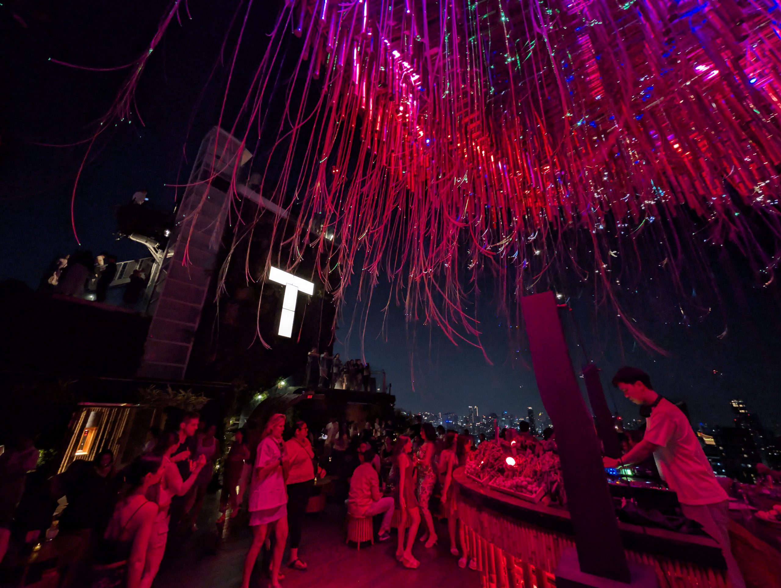 La estructura de luces LED rosas del techo del Tichuca Rooftop Bar de Bangkok, con la gente y los rascacielos iluminados al fondo