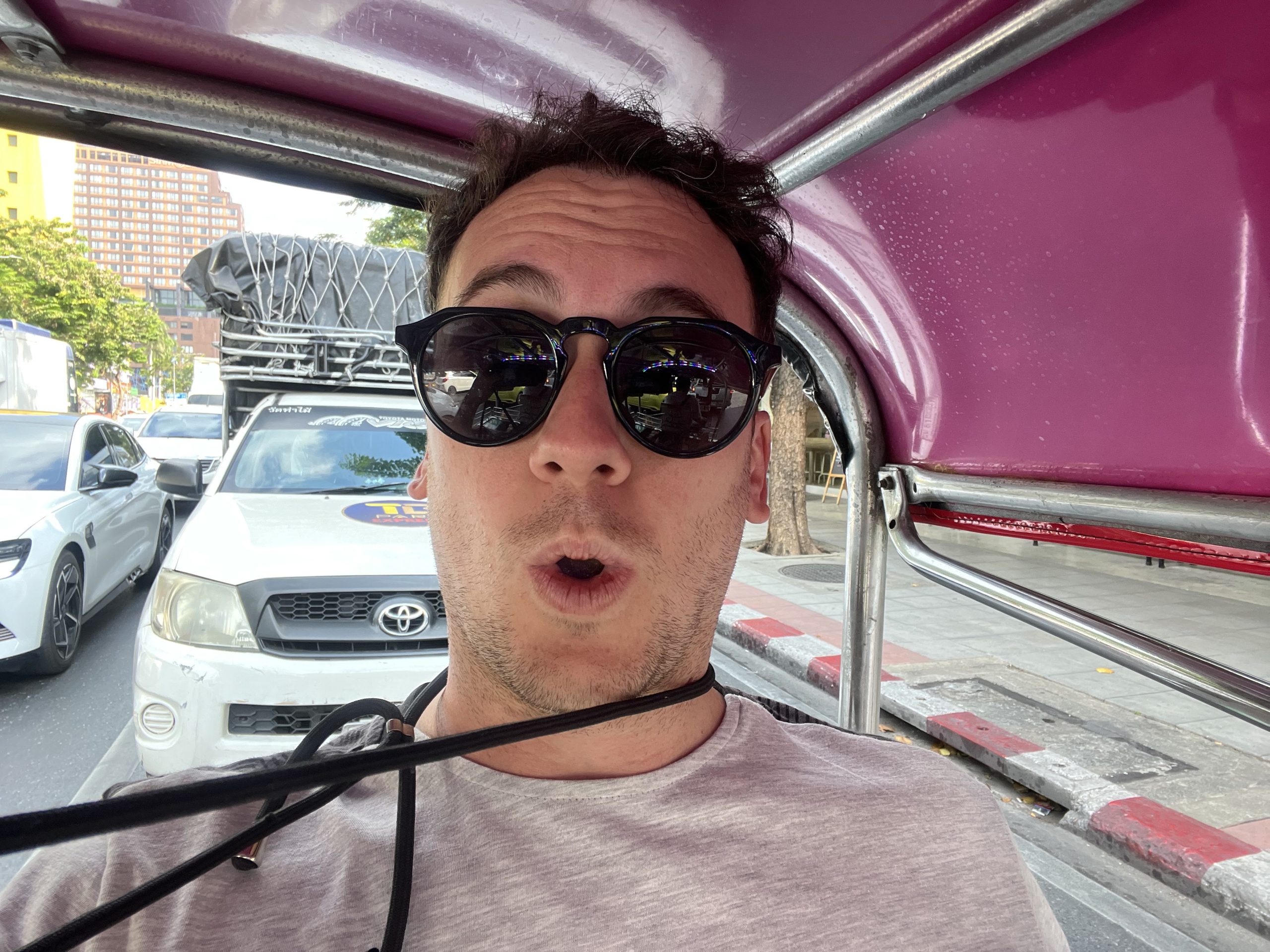 Víctor dentro de un tuk-tuk de techo rosa en Bangkok, con cara de susto y los coches pegados al lado