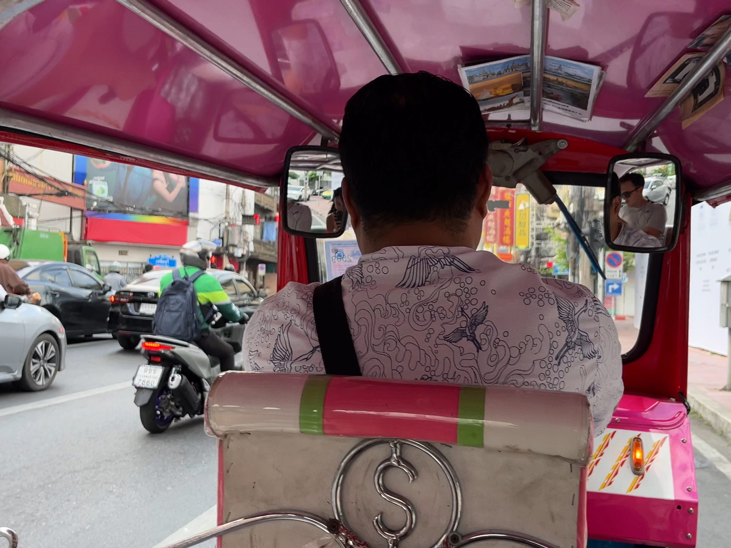 Vista desde el asiento trasero de un tuk-tuk en Bangkok, con el conductor delante y motos y coches alrededor