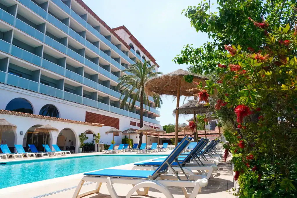Luxurious hotel pool area with sun loungers, umbrellas, and lush tropical plants.