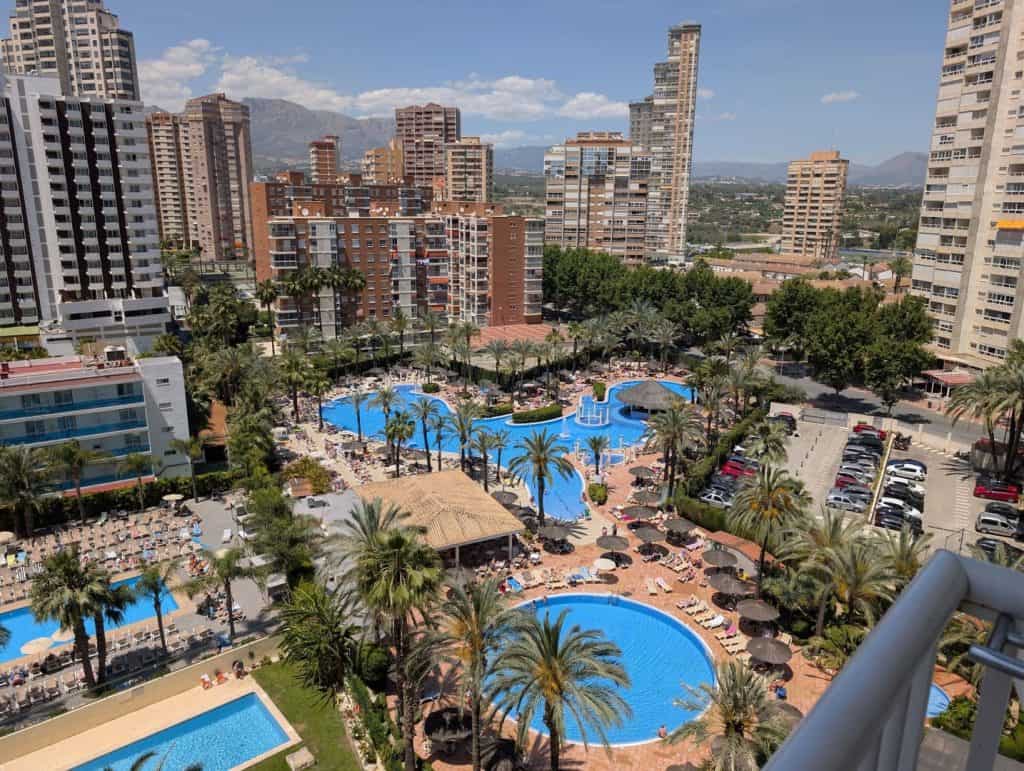 A lush hotel pool area with palm trees surrounded by high-rise buildings in an urban setting.