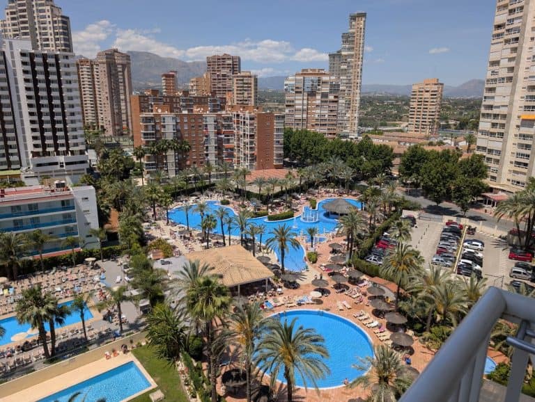A lush hotel pool area with palm trees surrounded by high-rise buildings in an urban setting.