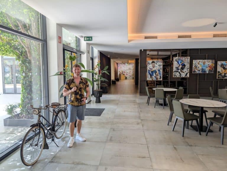 A woman standing inside a modern hotel lobby with a bicycle and artwork on the walls.