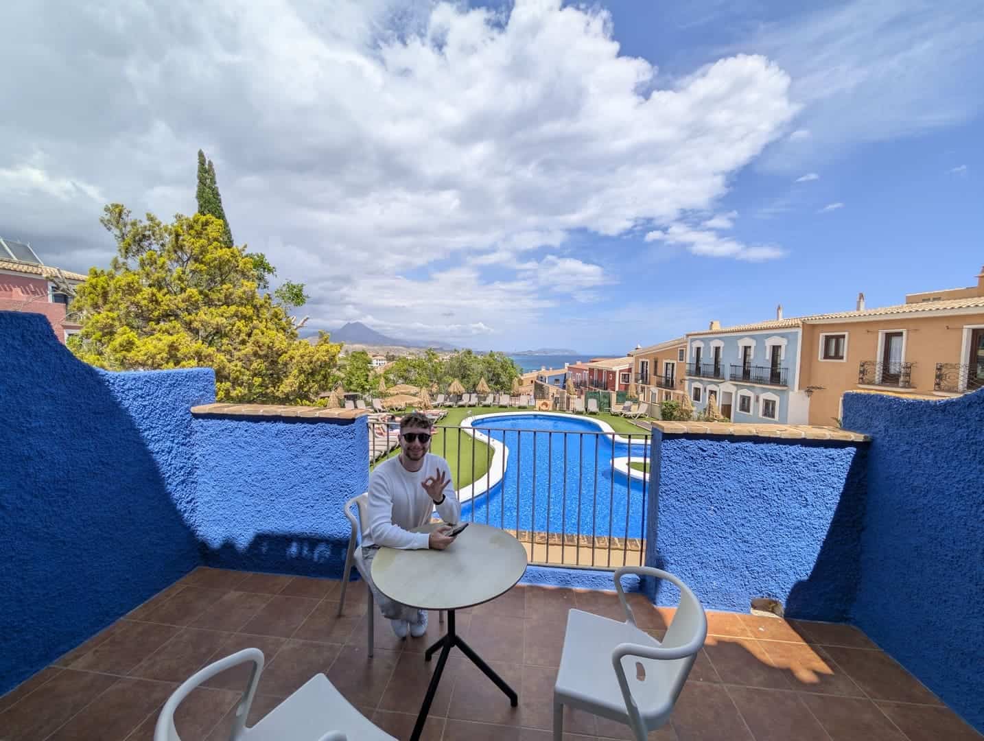 Javier Sobrino sentado en la terraza de paredes azules de su habitación del Occidental Pueblo Acantilado, con la piscina y el mar al fondo