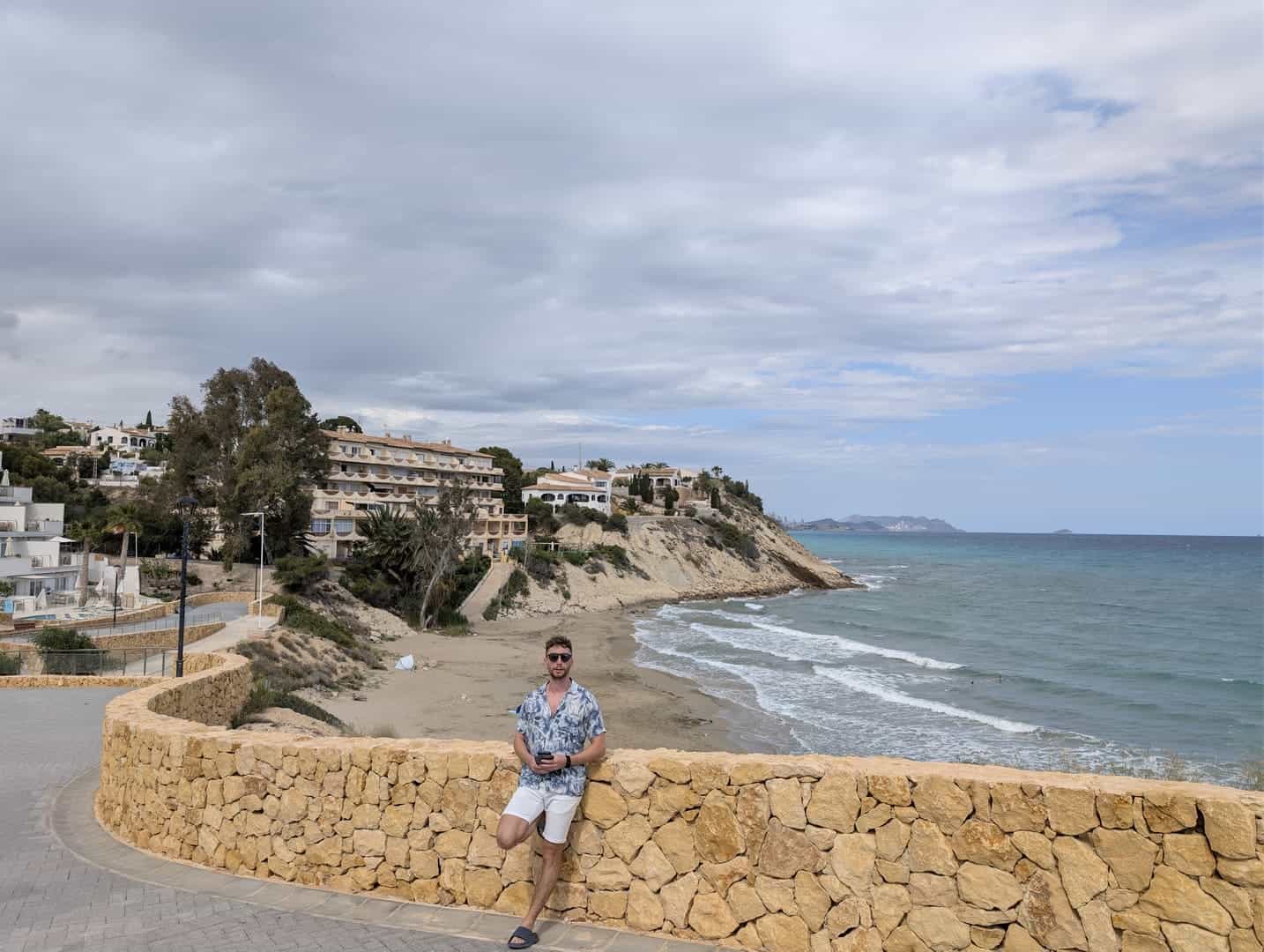 Javier Sobrino apoyado en un muro de piedra frente a una cala de arena de la zona de El Campello