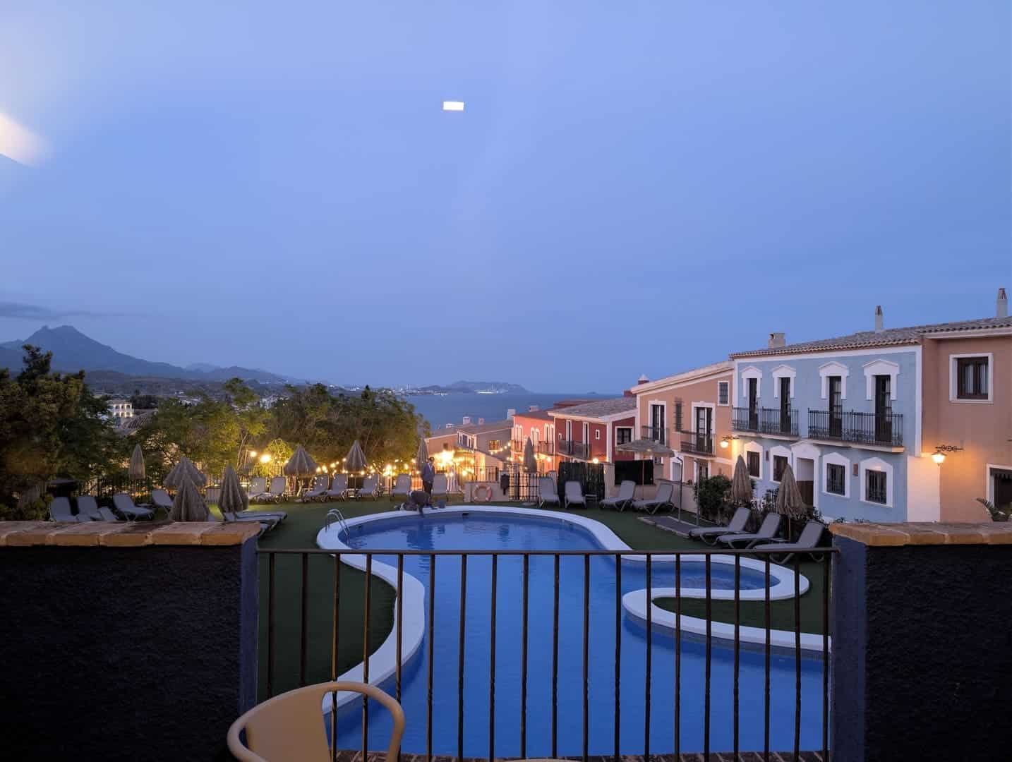 La piscina del Occidental Pueblo Acantilado al anochecer, con las luces encendidas y la sierra al fondo
