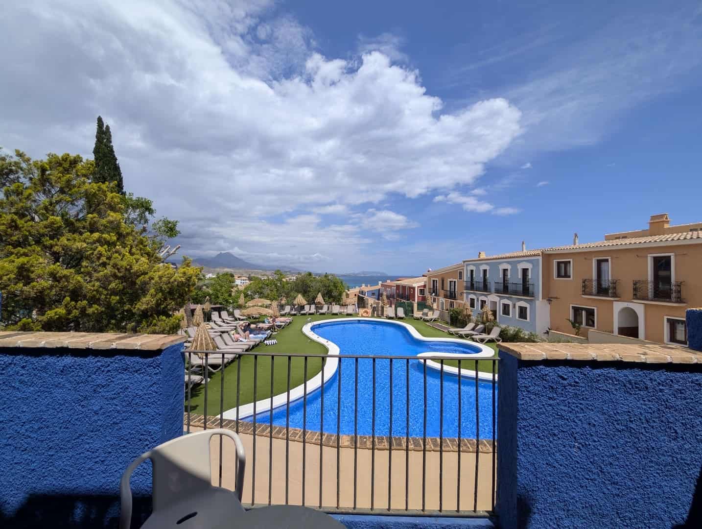 La piscina del Occidental Pueblo Acantilado vista desde una terraza azul, con el mar y la sierra detrás