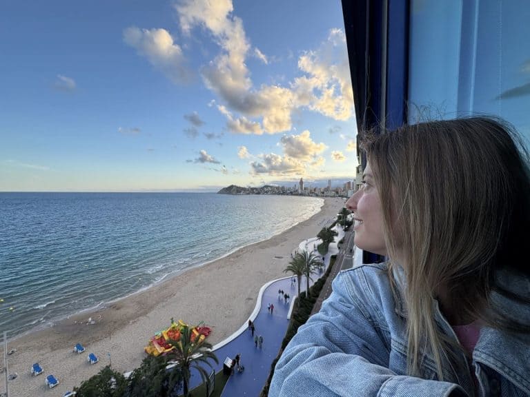 A woman enjoying a seaside view from a high-rise hotel window with a beach and city skyline in the b.