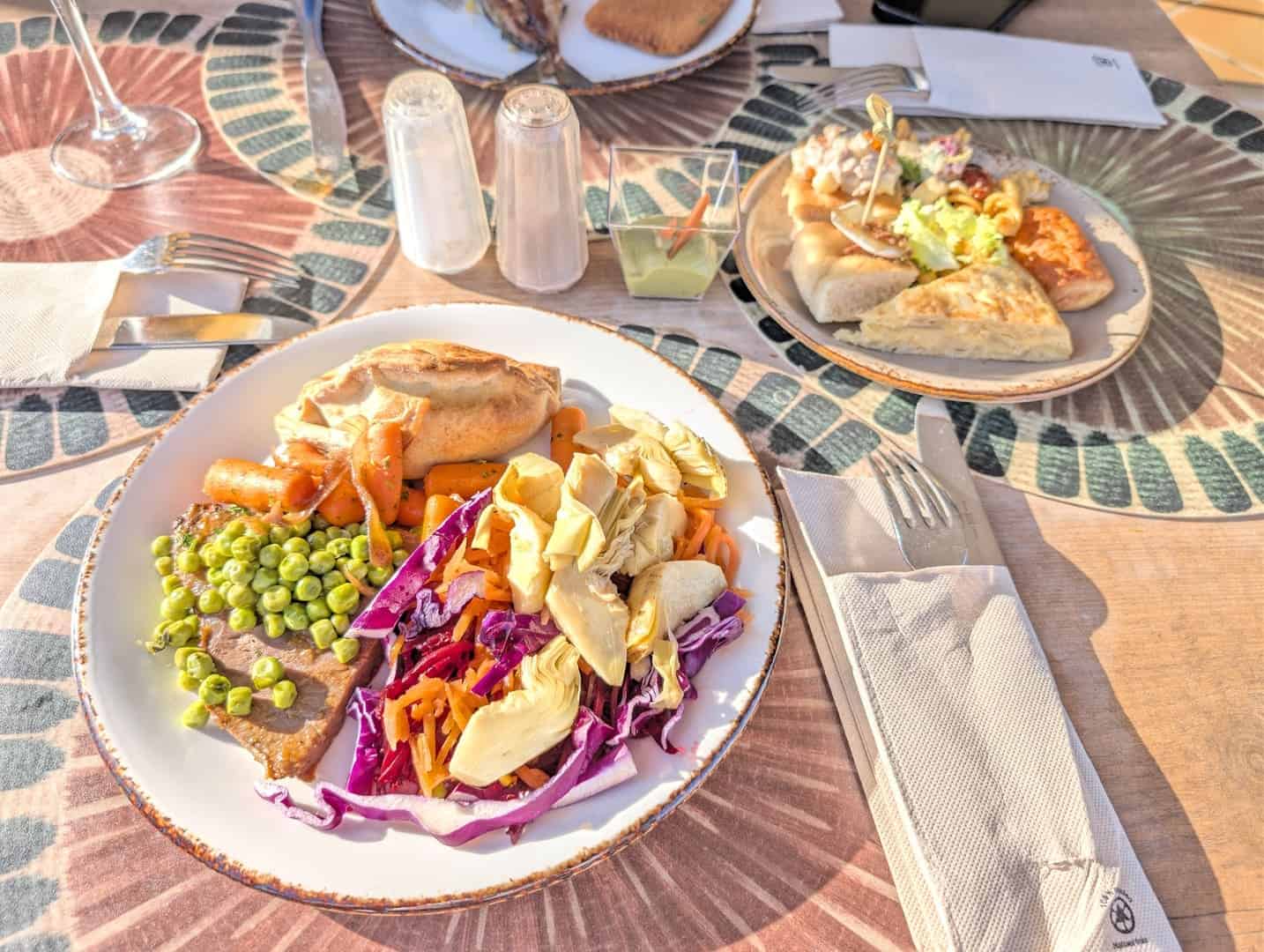 A colorful plate of mixed vegetables, chicken, and salad on a dining table with bread and condiments.