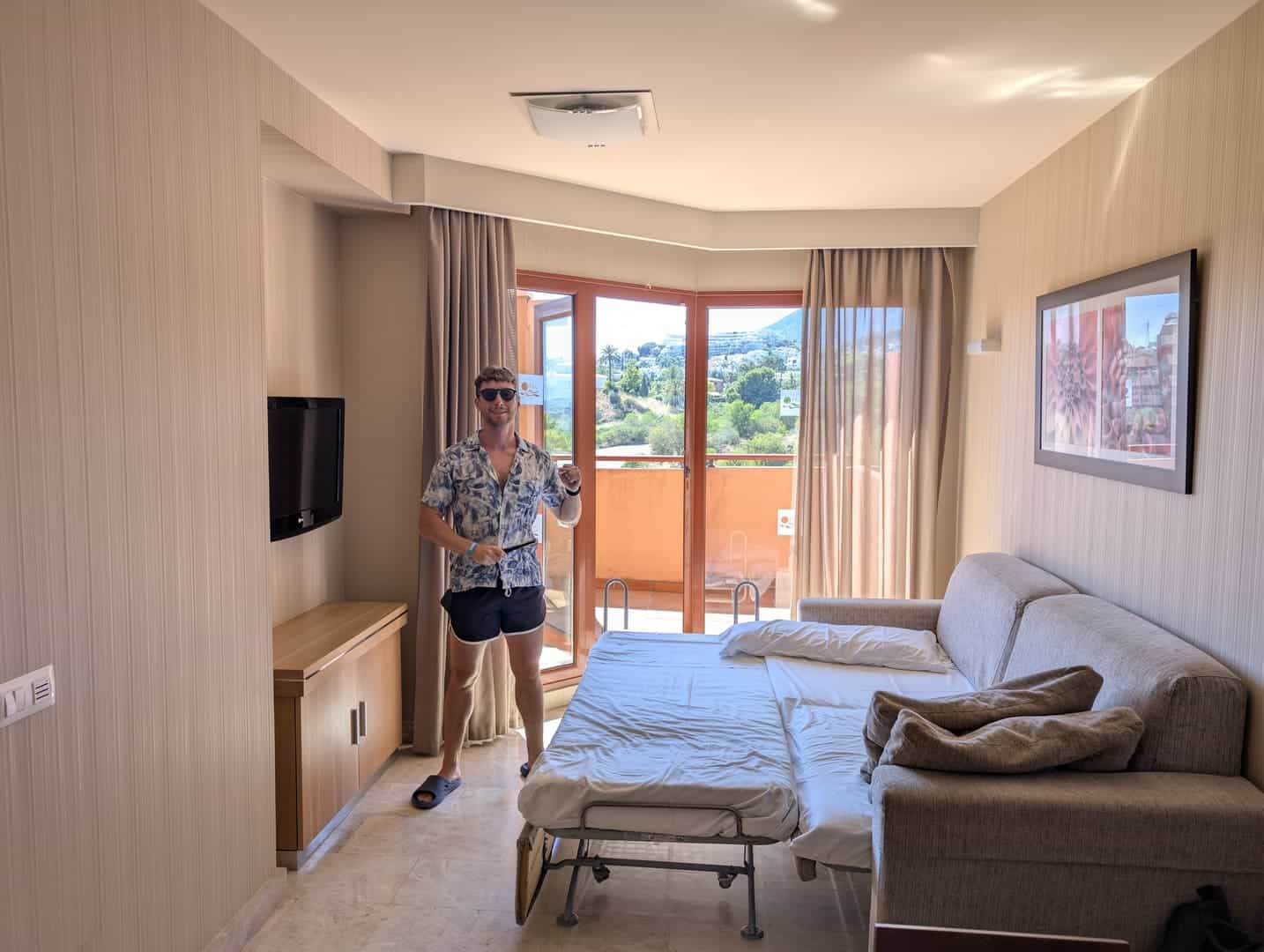A person standing in a hotel room with a balcony view of greenery and mountains.