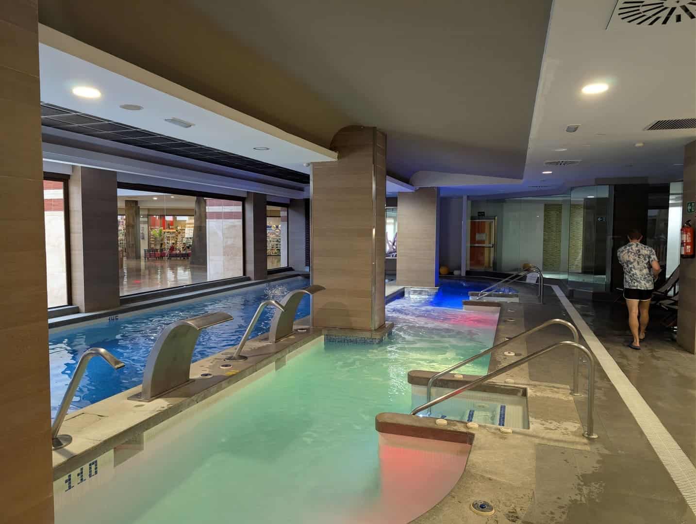 Relaxing indoor pool area with colorful lighting and modern design at a hotel spa.