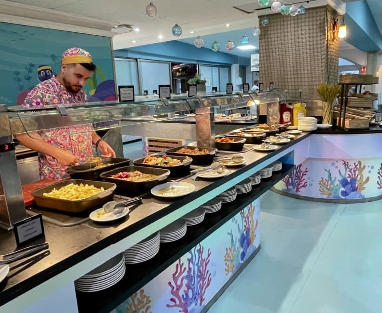 Mostrador largo del buffet del Magic Fantasy con el mural de coral y bandejas de comida