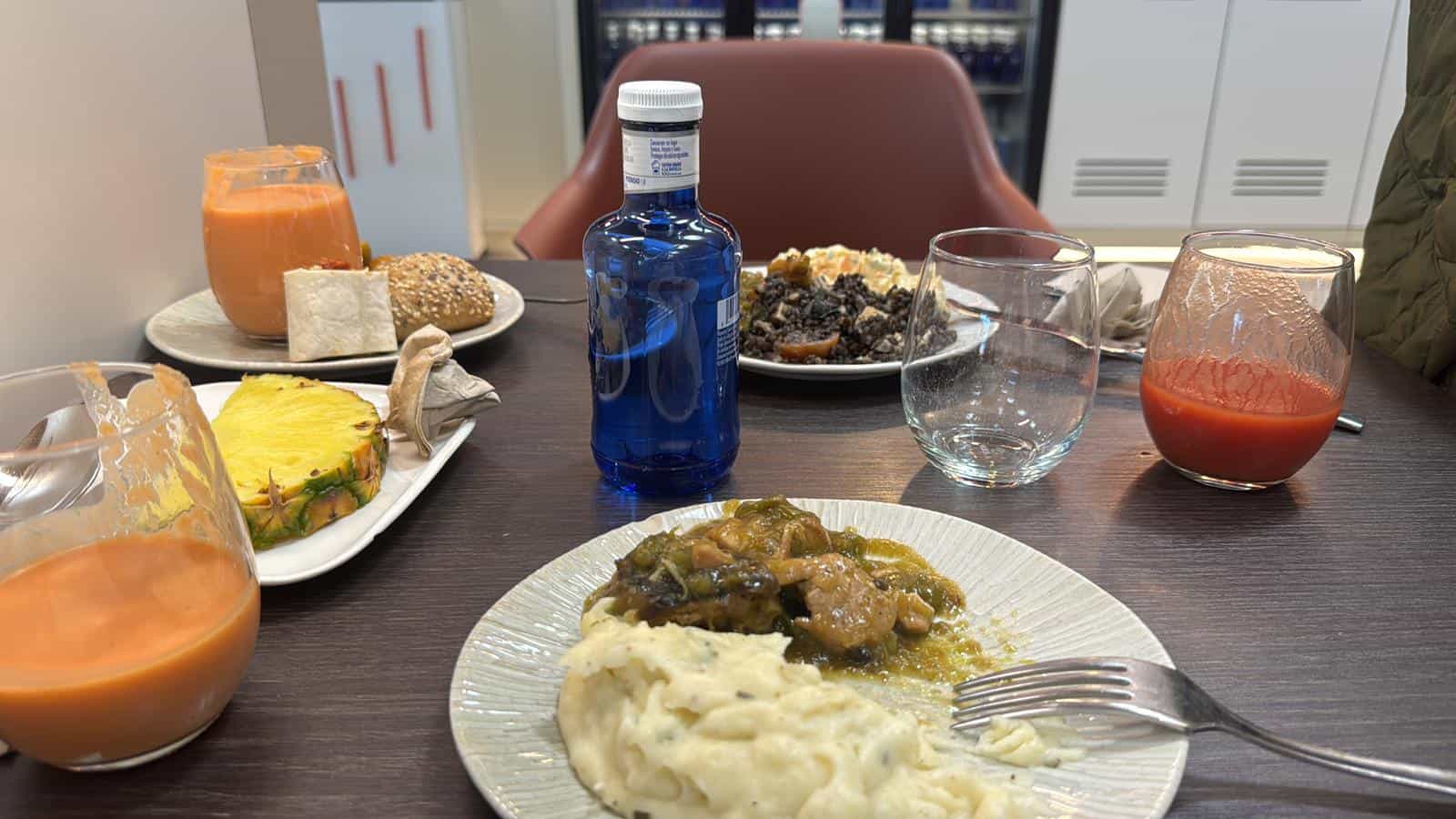 Mesa con varios platos de la sala VIP de Iberia: guiso con puré, ensaladas, gazpacho y una botella de agua