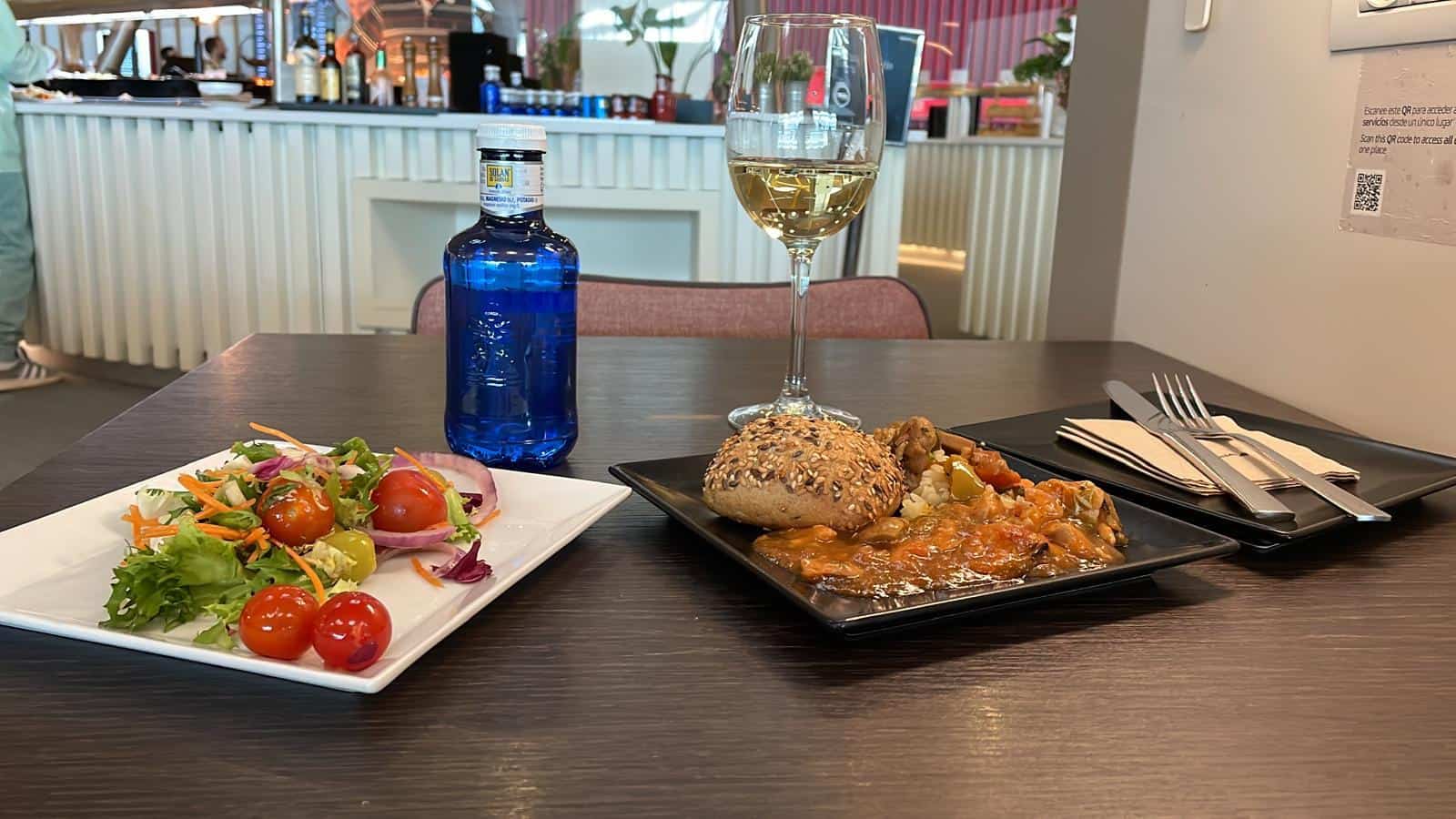 Plato de comida, ensalada y copa de vino blanco servidos en la sala VIP de Iberia del aeropuerto de Madrid
