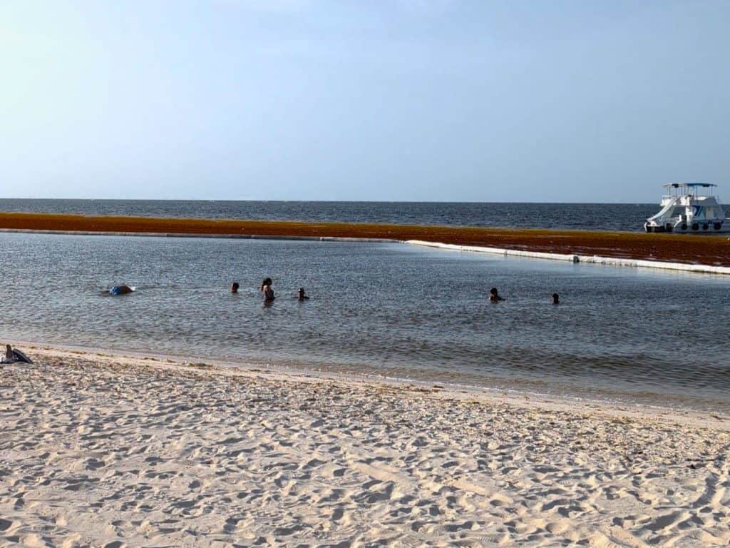 People swimming in a calm beach with a boat in the background.