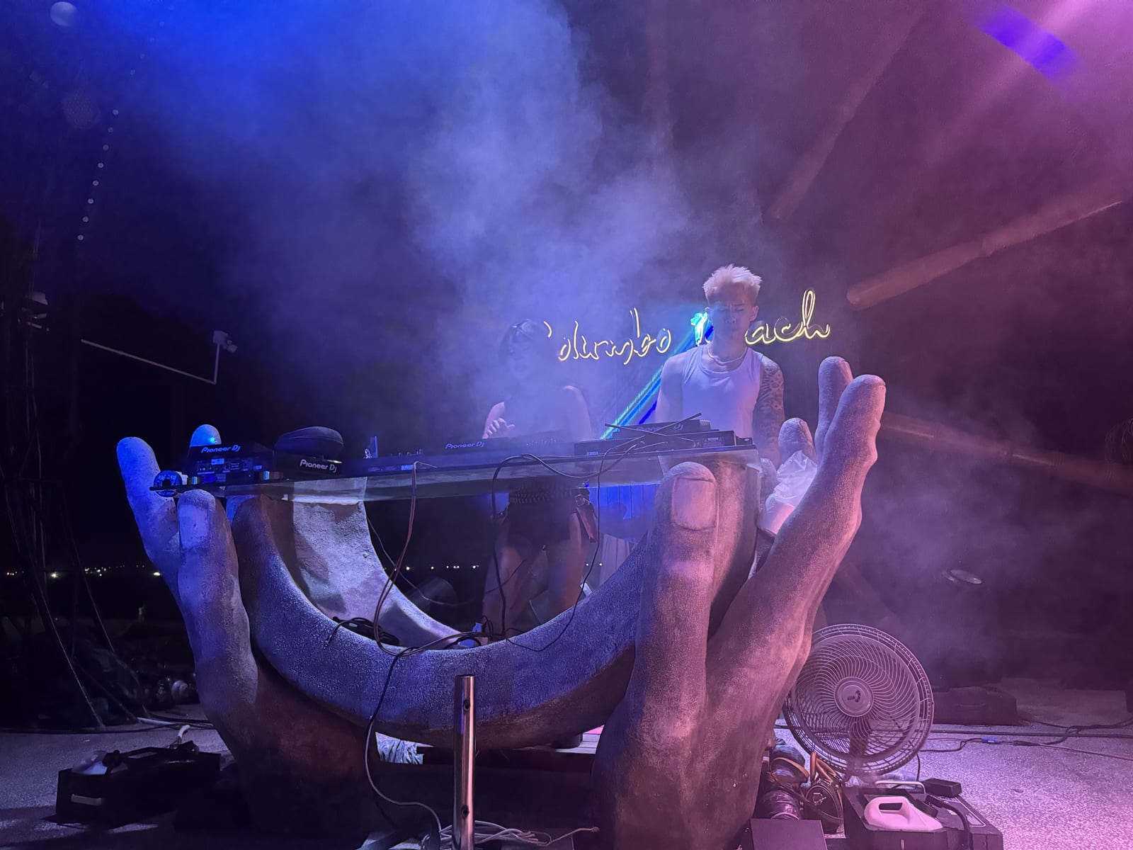 DJ pinchando de noche en un beach club de Da Nang, con la mesa sobre unas manos de hormigón