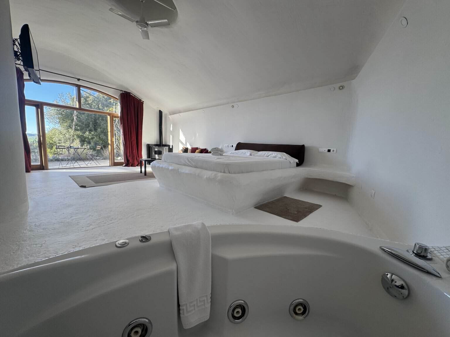 Cueva bioclimática del Hotel Spa Las Nubes con la cama, la estufa de leña y la bañera de hidromasaje en primer plano