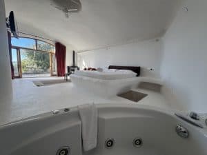 Spacious hotel room with a large bed, balcony, and jacuzzi in the foreground.