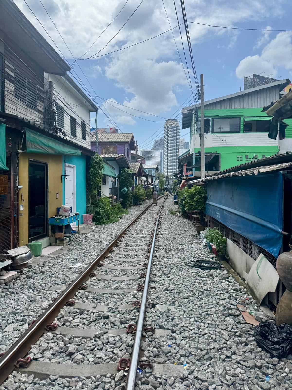 Vía de tren pasando entre casas bajas en Thung Maha Mek, en Sathorn, con rascacielos al fondo