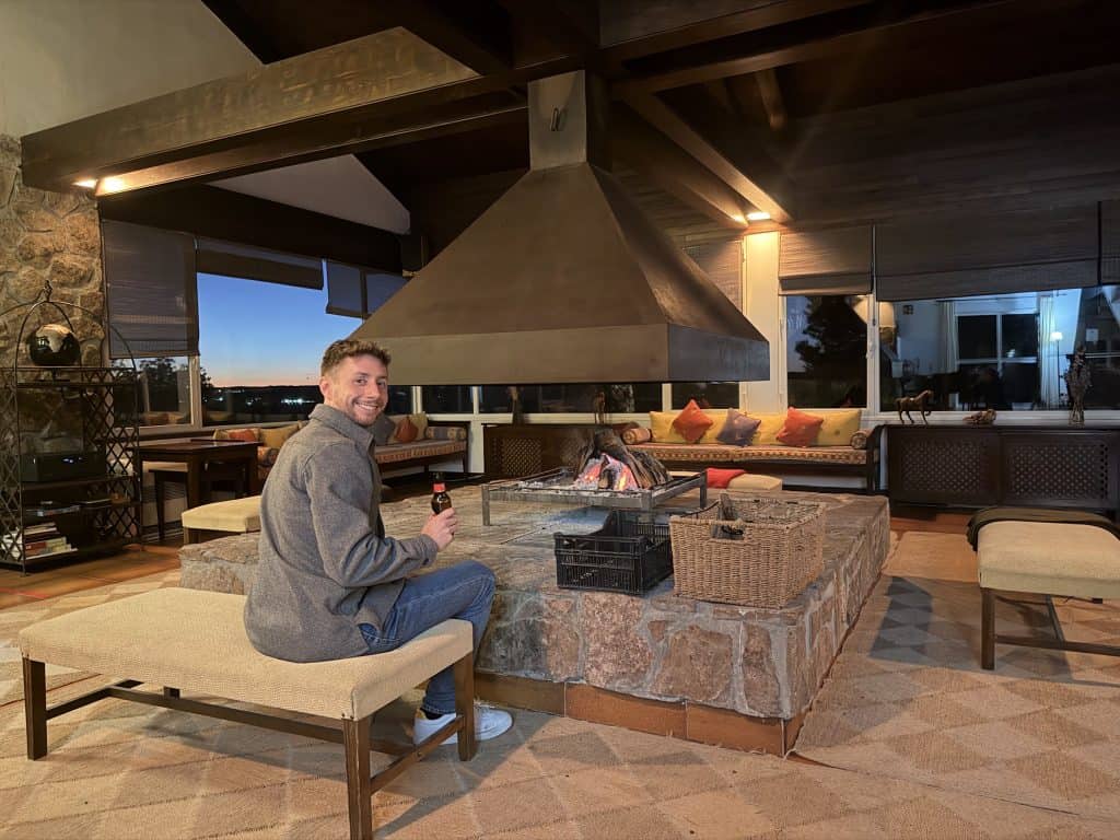 Salón común del Hotel Spa Las Nubes con la chimenea central de campana y las vistas al atardecer