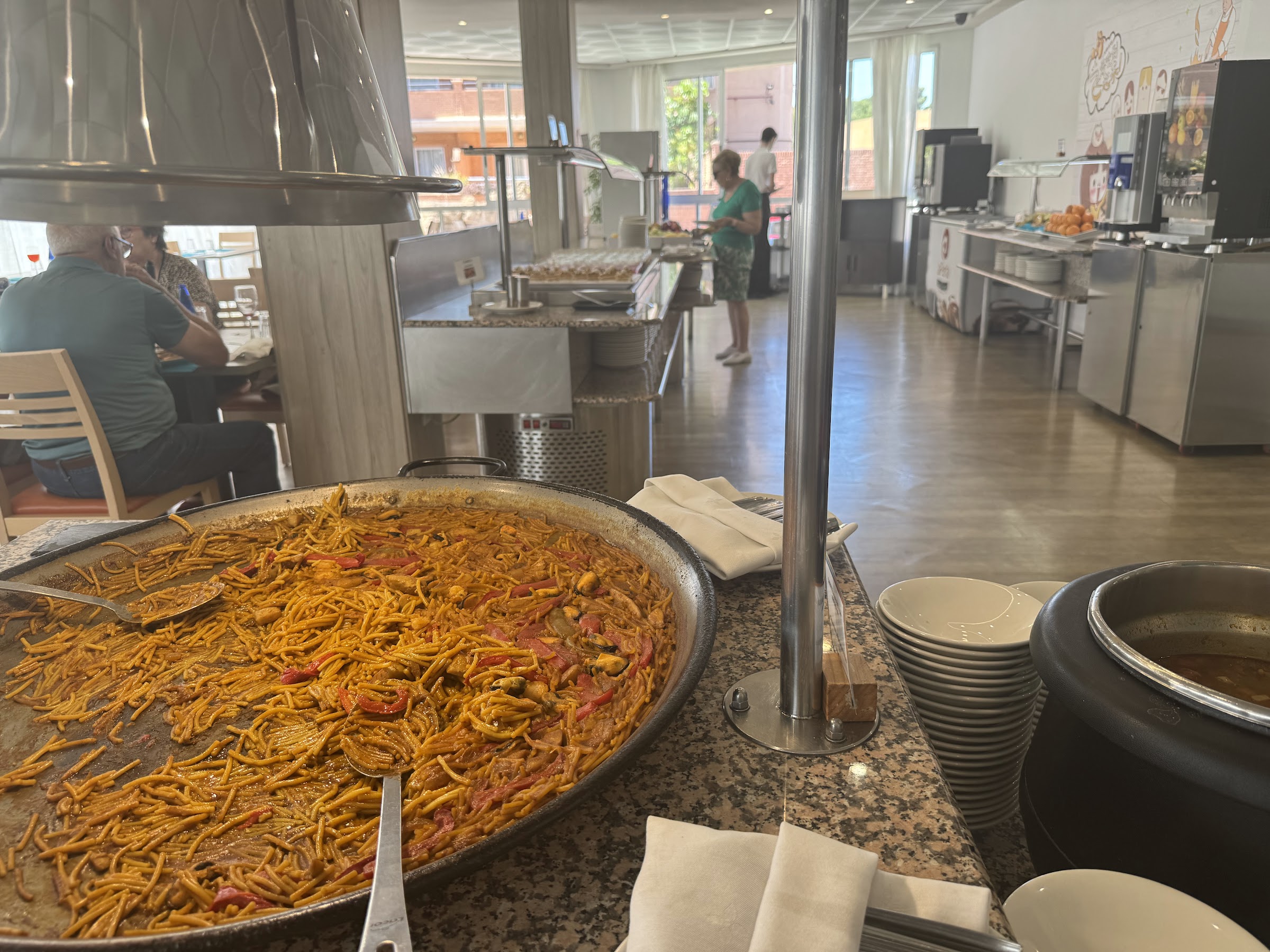 Paellera de fideuá en el buffet del Hotel Alone Benidorm con el comedor al fondo