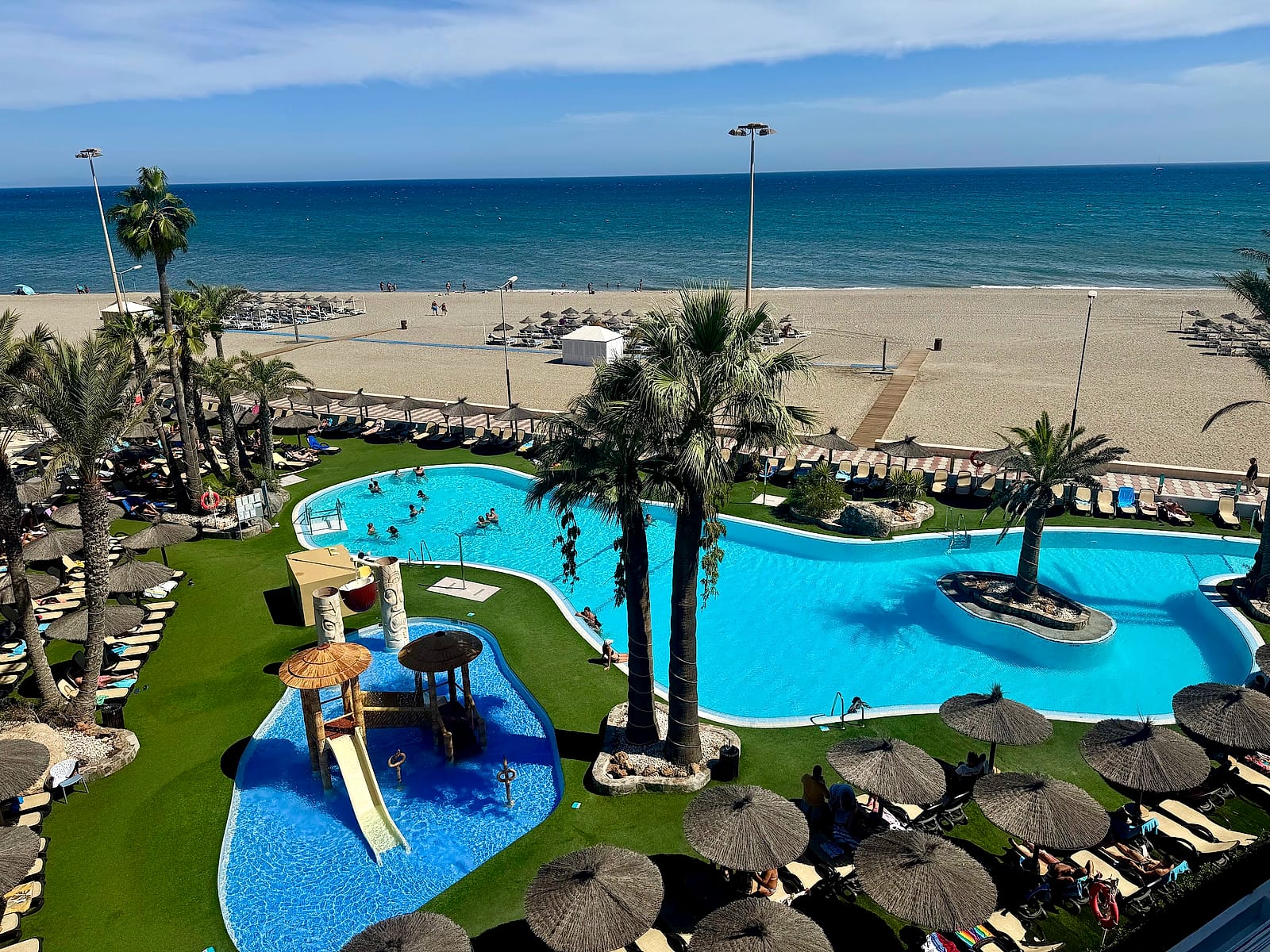 Vista desde arriba de las piscinas del Alua Golf Trinidad, con la playa y el mar detrás
