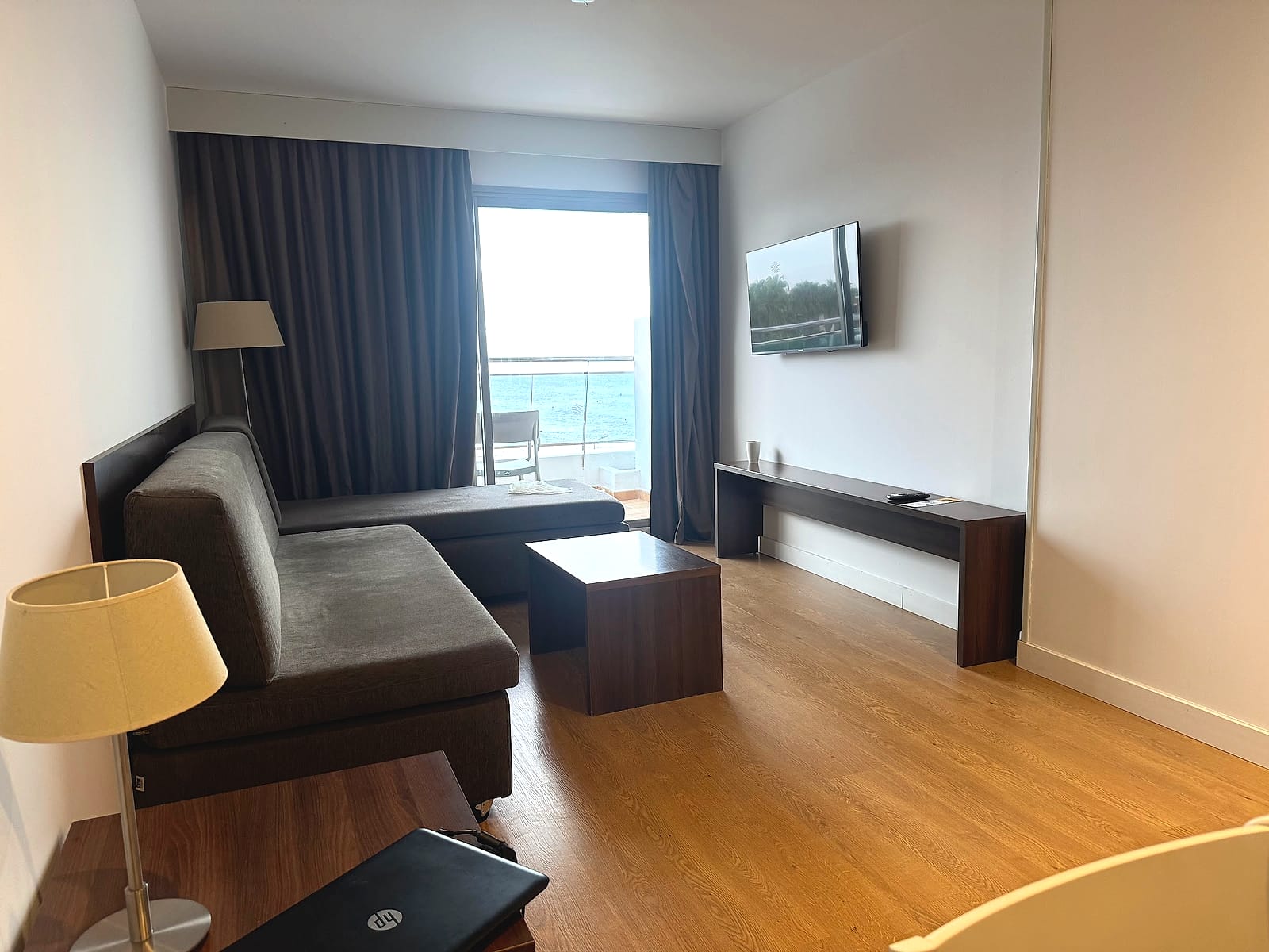 El salón de la suite del Alua Golf Trinidad, con sofá, televisión y el mar al fondo