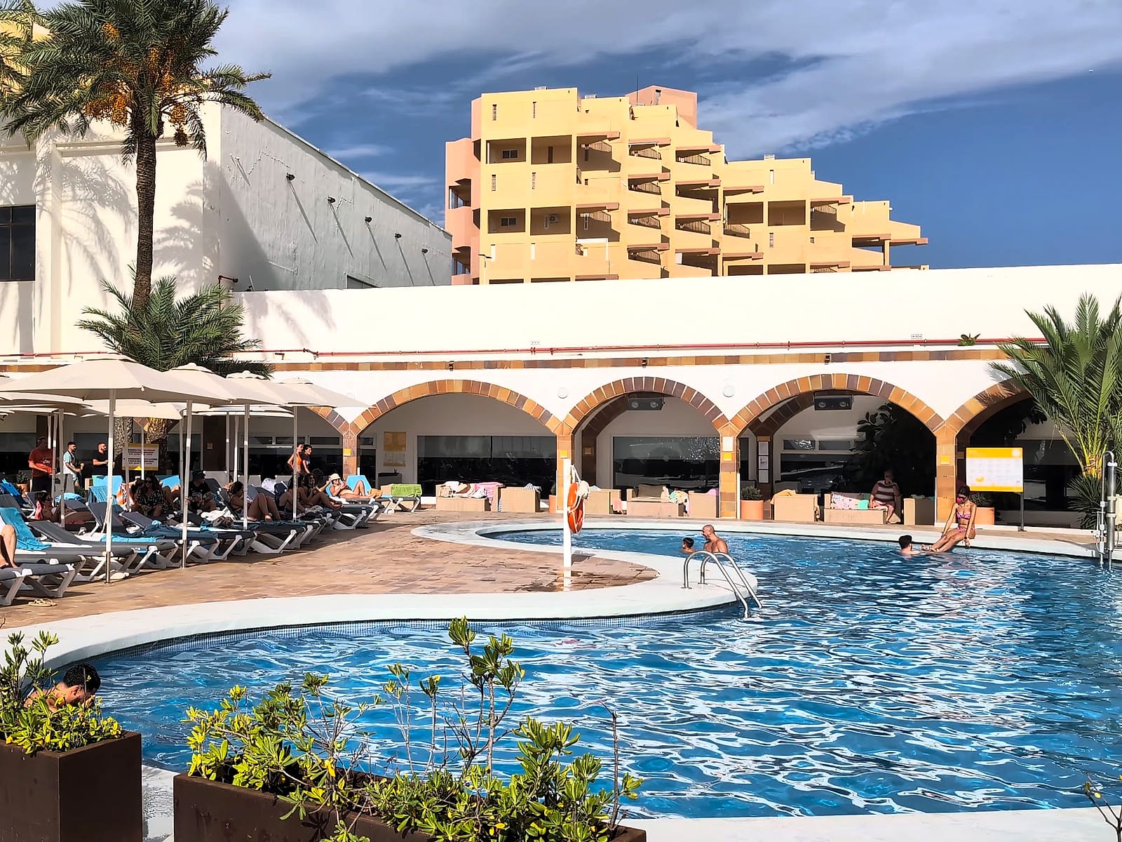 La piscina principal del AluaSun Doblemar, con los arcos del edificio bajo y las hamacas