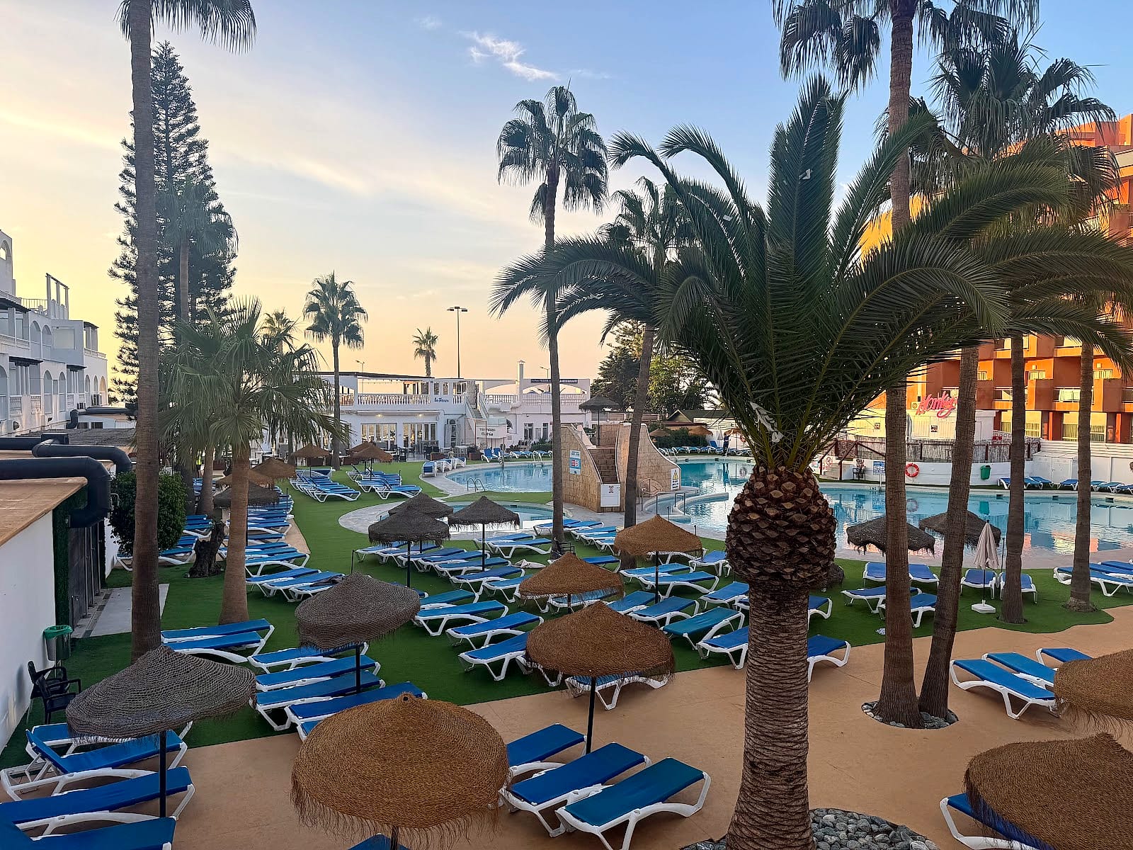 La zona de piscinas del Hotel Bahía Serena al atardecer, con palmeras, sombrillas y hamacas